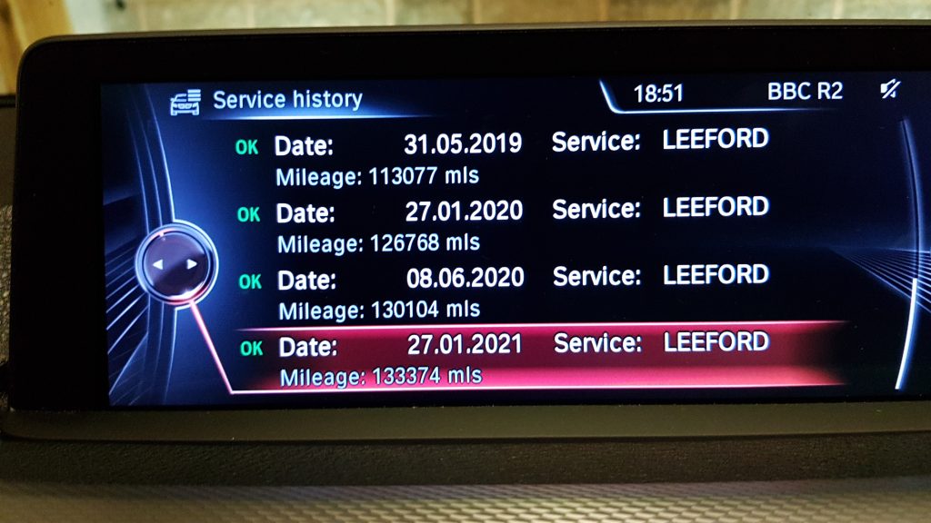 Car infotainment screen displaying service history with dates, mileage, and service location details