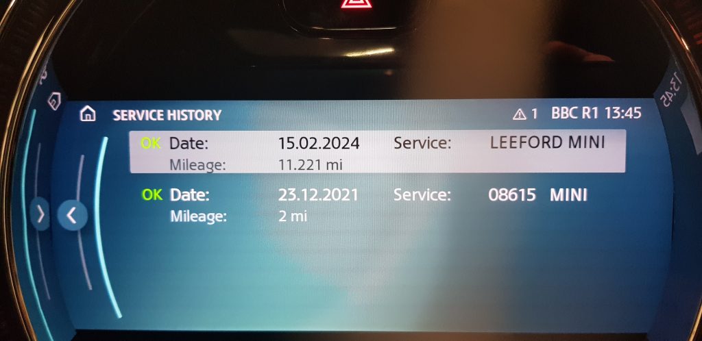Car dashboard display showing digital service history with recent service date, mileage, and dealership details